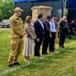 501050925_728989046143286_829013051419628686_n Grupa ludzi stoi w szeregu na zielonym trawniku. Mają na sobie różne mundury i ubrania formalne. W tle są bele siana i niebieski namiot.