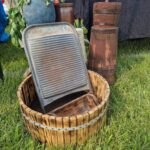 502617164_728062112902646_252662423016542970_n Drewniana tara leży na beczce na trawie, obok niej niebieski wazon i drewniane naczynia. W tle czarny stół i kolorowy bieżnik.