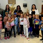 Grupa dzieci i dorosłych pozuje w muzeum. W tle znajdują się rzeźby i obrazy. Uśmiechy i radość w otoczeniu sztuki.