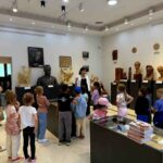 Grupa dzieci w muzeum z przewodnikiem. W tle popiersia i rzeźby, dominują jasne kolory ścian. Dzieci słuchają z zainteresowaniem.