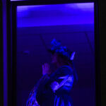 Na obrazie widać pierzastą postać w niebieskiej scenerii, podświetloną fioletowym światłem. Elementy kostiumu są bogate w detale i tekstury. Tło jest ciemne, co podkreśla sylwetkę.