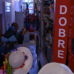 Wąskie wnętrze strażnicy z czerwoną ciężarówką po prawej. Ludzie w kapeluszach przyglądają się wyposażeniu. Szara ściana w tle.