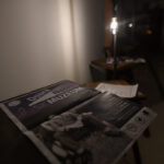 Na zdjęciu jest plakat promujący wydarzenie w muzeum. Jest w ciemnych odcieniach z fioletowymi akcentami. W tle widać słabo oświetlone pomieszczenie.