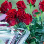 Bukiet czerwonych róż obok srebrnej tacy na zielonym tle. Kwitnące kwiaty mają intensywny kolor, a liście są ciemnozielone.