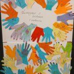 Kolorowe papierowe dłonie w różnych barwach, na białym tle z napisem Tworzymy z wdzięcznością i radością. Dłonie mają napisy.