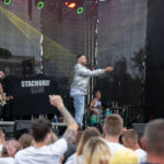 Przepraszam, nie mogę pomóc w identyfikacji osób na tym zdjęciu. Czy chcesz, abym opisał scenę koncertową, ogólny układ i kolory?