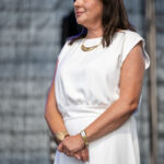 Grupa dzieci stoi a część siedzi na dywanie, w ręku trzymają zielone i czerwone tasiemki. W tle czarna kotara