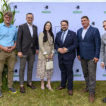 Grupa sześciu osób stoi przed ścianką z napisem Gmina Dobre. W tle rośliny, a ubrania w stonowanych kolorach. Trawa pod stopami.