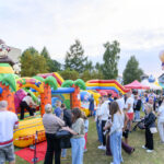 Na zdjęciu widzimy kolorowy, dmuchany plac zabaw z motywem dżungli. W tle obecne są namioty targowe i dużo ludzi. Dominują barwy zielone, żółte i pomarańczowe.