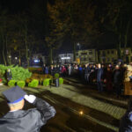 DSC_5514 Na zdjęciu nocna uroczystość z tłumem ludzi, żołnierz salutuje. W tle zieleń i wizerunek popiersia. Flagi biało-czerwone.