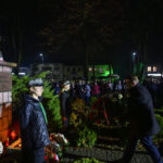 DSC_5545 Pomnik Marszałka Piłsudskiego otoczony wianuszkiem. Tło nocne, podświetlone na zielono budynki i zgromadzeni ludzie. Osoby w historycznych mundurach składają hołd.