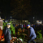 DSC_5558 Pomnik Piłsudskiego otoczony kwiatami i ludźmi w mundurach. Nocne tło z drzewami, delikatne oświetlenie. Ludzie zgromadzeni wokół.