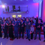 DSC_5779 Sala wypełniona ludźmi świętującymi, trzymającymi polskie flagi. Dominują kolory czerwony, biały i niebieski. W tle widoczny balkon z osobami filmującymi.