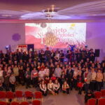 DSC_5846 Duża grupa ludzi w sali z flagami Polski, świętująca 11 listopada. Dominują biało-czerwone kolory. W tle widoczny baner z napisem „Święto Niepodległości”.