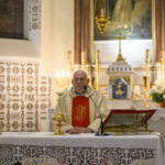 DSC_7768 Kapłan w złotym ornacie stoi za ołtarzem, na którym znajduje się kielich. W tle obrazy religijne, świece i złote ozdoby. Wnętrze kościoła jest jasne i bogato zdobione.