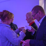 DSC_7915 Cztery osoby ściskają wstążki na przyjęciu. Dominują niebieskie światło i półmrok. W tle widać stół z kwiatami i świecami.