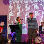 DSC_8033 Koncert przed historycznym zdjęciem żołnierzy, śpiewają kobieta w zielonej sukni i mężczyzna w mundurze, w tle perkusista.