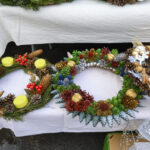 Kolorowe wieńce świąteczne z szyszek, gałązek, złotych i czerwonych ozdób. Na białym obrusie. W tle ciemne tło.