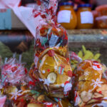 Przezroczysta torebka z suszonymi owocami i świątecznymi motywami. W tle słoiki i ozdobne tło. Dominują czerwienie i pomarańcze.