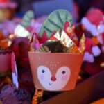 Świąteczne muffinki w ozdobnych papilotkach. Motyw renifera i złotych dekoracji. Tło zamazane, rozmyte w świątecznych kolorach.