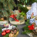 Świąteczna kompozycja z gałązkami jodły, czerwonymi ozdobami i szyszkami na drewnianych podstawach. Dominuje zieleń i czerwień. Tło ciemne, dodające kontrastu.