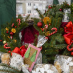 Świąteczne wieńce z igliwia, ozdobione czerwonymi kokardami, cukierkami i suszonymi pomarańczami. Tło zielone. Są też zapakowane w folię pierniki i kartki świąteczne.