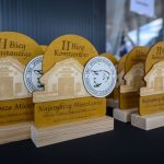 DSC_5346 Złote statuetki z napisem II Bieg Konstantego na drewnianej podstawie. Obok medal z wizerunkiem mężczyzny. Tło jest niebieskie.