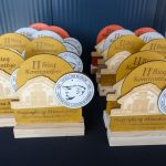 DSC_5349 Na zdjęciu widać drewniane trofea z napisem II Bieg Konstantego na czarnym stole. Trofea mają okrągły emblemat z rysunkiem budynku i portretem. W tle widoczne są podobne nagrody w kolorach żółtym, pom