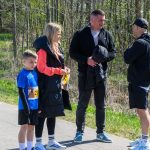 DSC_5357 Na zdjęciu jest grupa czterech osób na ścieżce, na tle zieleni i drzew. Mężczyźni są ubrani na ciemno, chłopiec ma niebieską koszulkę. Obok nich jest kobieta w czarnej kurtce, rozmawiają.