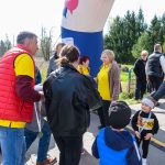 DSC_5418 Grupa ludzi w kolorowych ubraniach stoi obok dużego dmuchanego łuku. W tle widać drzewa. Jasny dzień na zewnątrz.