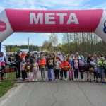 DSC_5468 Dzieci stoją na linii startu pod różowo-niebieskim łukiem z napisem META. Tło stanowi zieleń i zebrani ludzie. Słoneczny dzień, jasne kolory.