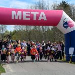 DSC_5476 Zdjęcie przedstawia start biegu dzieci pod różowo-niebieskim łukiem z napisem META. W tle widoczni są kibice oraz drzewa. Na niebie znajdują się białe chmury.
