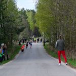 DSC_5491 Bieg dzieci na wiejskiej drodze między drzewami wiosną. W tle kibicujący dorośli, dzieci w kolorowych ubraniach. Pogoda jasna, pochmurna.