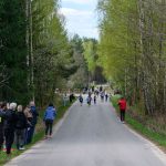 DSC_5548 Na zdjęciu bieg uliczny dzieci na wiejskiej drodze. Wokół zielone drzewa i kibice. Pogoda jest pochmurna.