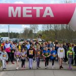 DSC_5575 Zdjęcie przedstawia start biegu dzieci pod różowym łukiem z napisem META. W tle zieleń i zaparkowane samochody. Grupa młodych uczestników stoi na starcie, gotowa do biegu.