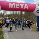 DSC_5647 Biegacze startują spod różowo-białej bramy z napisem META. W tle drzewa i widownia. Pogoda jest pochmurna.