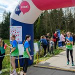 DSC_5673 Biegaczka w niebiesko-zielonym stroju mija nadmuchaną bramę z napisem „Ale czas!”. W tle drzewa i kibice. Słoneczny dzień.