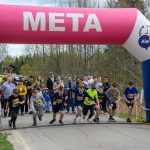 DSC_5681 Na zdjęciu grupa dzieci startuje w biegu spod różowego łuku z napisem „META”. Tło stanowi zalesiony krajobraz, a z boku stoi tłum ludzi. Widoczna jest tablica z czasem 0:00:00.