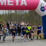 DSC_5683 Grupa dzieci startuje w biegu spod różowego łuku z napisem META. W tle są drzewa i tłum ludzi. Dzień jest pochmurny.