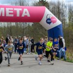 DSC_5685 Na zdjęciu grupa dzieci startuje w biegu pod różowym łukiem z napisem META. Tło stanowią drzewa i kibicujący ludzie. Dzieci mają na sobie kolorowe stroje sportowe.