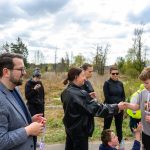 DSC_5732 Grupa ludzi na zewnątrz, chłopiec w koszulce z numerem 265 otrzymuje gratulacje. W tle drzewa i pochmurne niebo.