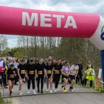 DSC_5745 Start biegu pod różowo-białym łukiem z napisem META. Grupa zawodników stoi na starcie. W tle drzewa i widzowie.