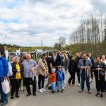 DSC_5761 Grupa ludzi stoi na asfaltowej drodze, kilka osób trzyma medale. W tle widoczne są drzewa i pochmurne niebo. Po lewej stronie znajduje się drewniany pawilon.