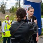 DSC_5786 Grupa ludzi rozmawia na tle niebieskiego balonu startowego. Jedna z osób ma żółtą kamizelkę odblaskową. W tle widać zieleń i niebo.