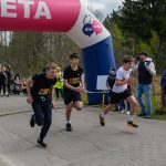 DSC_5813 Trzech mężczyzn biegnie przez metę. Nad nimi różowy łuk z napisem META. W tle widoczni kibice i drzewa.