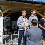 DSC_5947 Trzech młodych sportowców na podium z medalami, w tle drewniana altana i baner Mazowsze. Kolory szary, niebieski i czerwony dominują na zdjęciu.