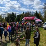 DSC_5955 Na zdjęciu widnieje tłum ludzi na starcie biegu, z różnokolorowymi koszulkami. Nad nimi różowy łuk z napisem START. W tle drzewa i niebo z chmurami.