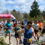 DSC_6013 Biegacze przekraczają różowo-białą metę, a za nimi widać las i błękitne niebo. Kolorowe stroje uczestników. Spokojna atmosfera.