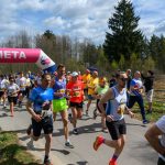 DSC_6016 Biegacze przekraczają różowy łuk z napisem META. Mają kolorowe stroje sportowe. Tło to drzewa i niebo z chmurami.