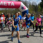 DSC_6067 Grupa ludzi w sportowych strojach z kijkami przekracza linię mety. Nad nimi różowo-biały łuk z napisem META. W tle widać drzewa i niebo.